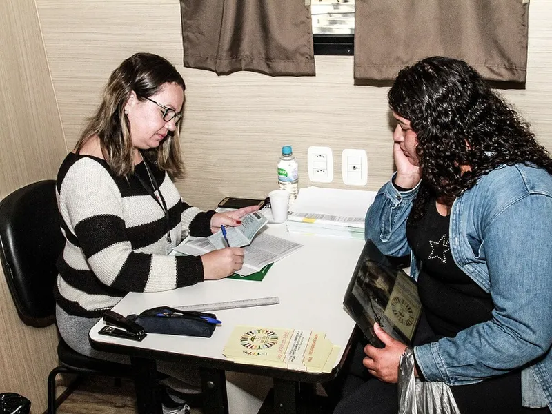 Assistente social em atendimento, conversando com uma mulher sentada à mesa