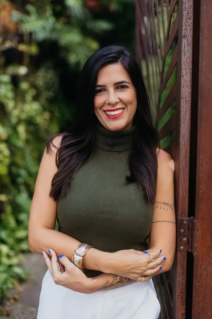 Tamara Almeida sorrindo, com plantas ao fundo.