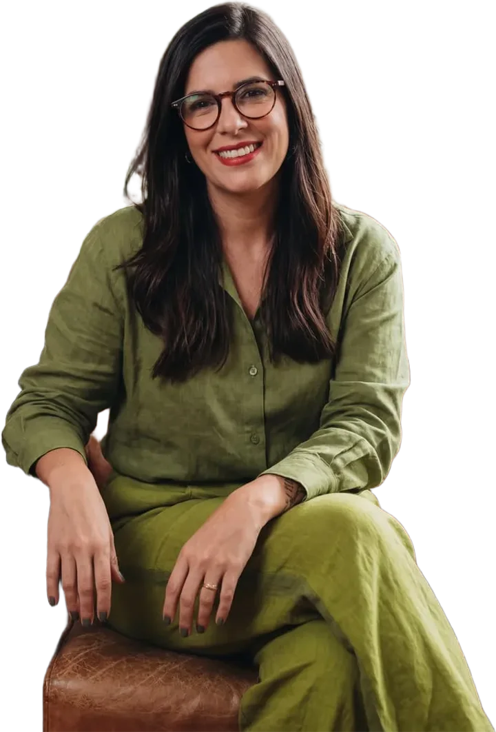 Tamara Almeida sorrindo, sentada, de óculos e conjunto verde